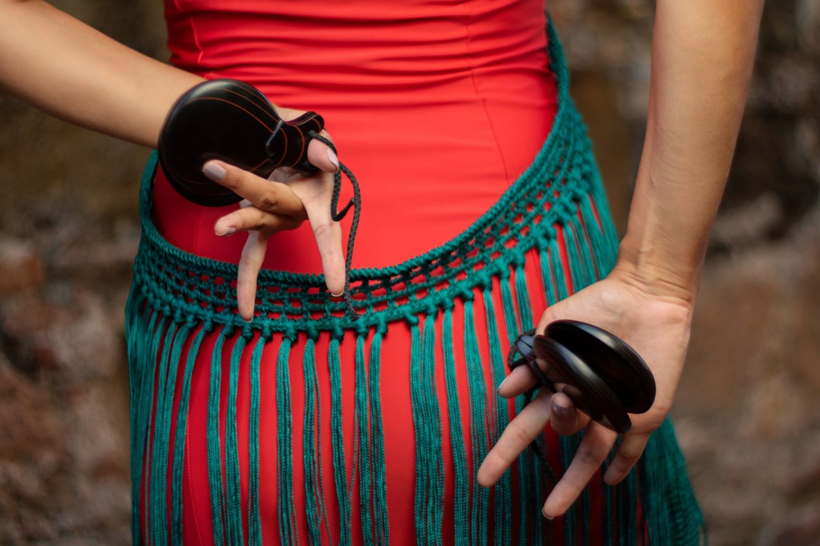 A close-up of a dancer's hands holding castanets with a colorful costume detail