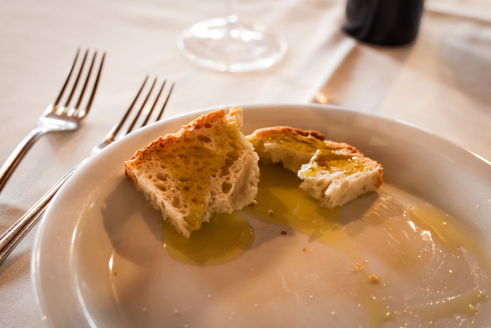 Close-up of bread with olive oil on a white plate at a restaurant table setting