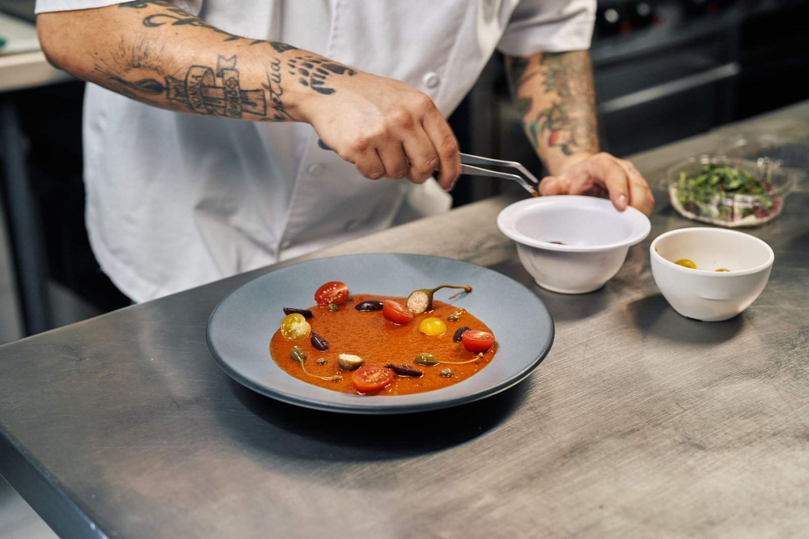 Chef expertly garnishing a tomato soup with cherry tomatoes and herbs in a professional kitchen