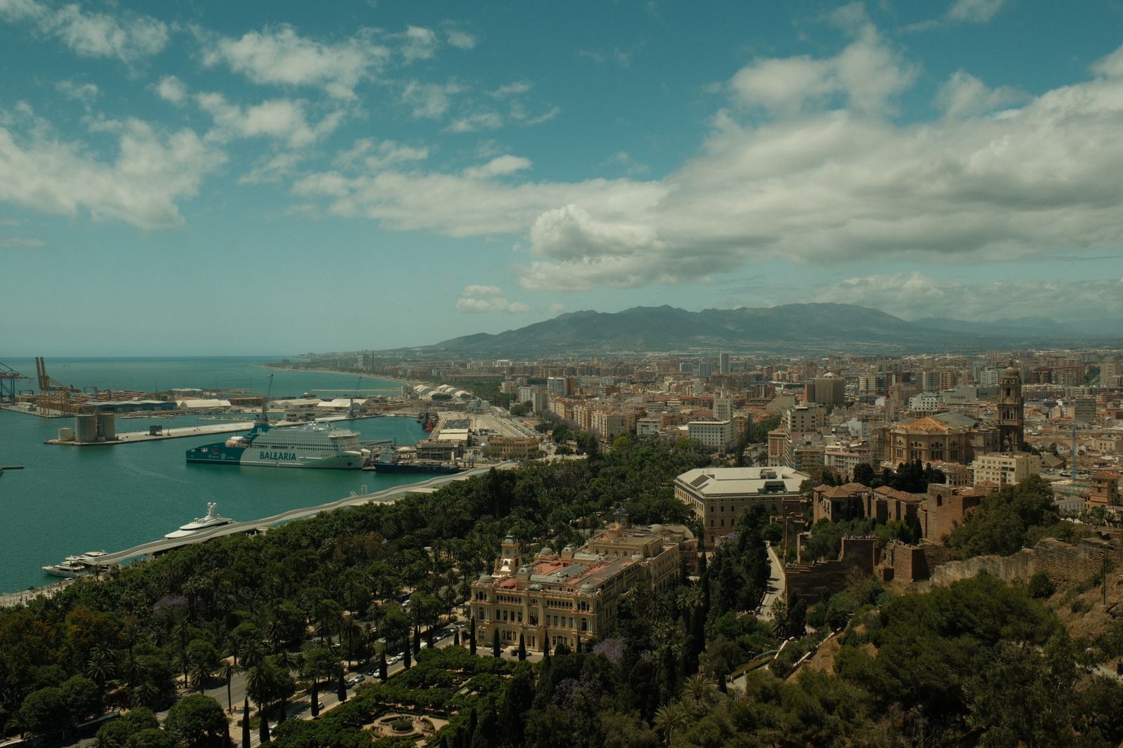 A scenic view of Málaga's harbor and city against a mountainous backdrop under a partly cloudy sky