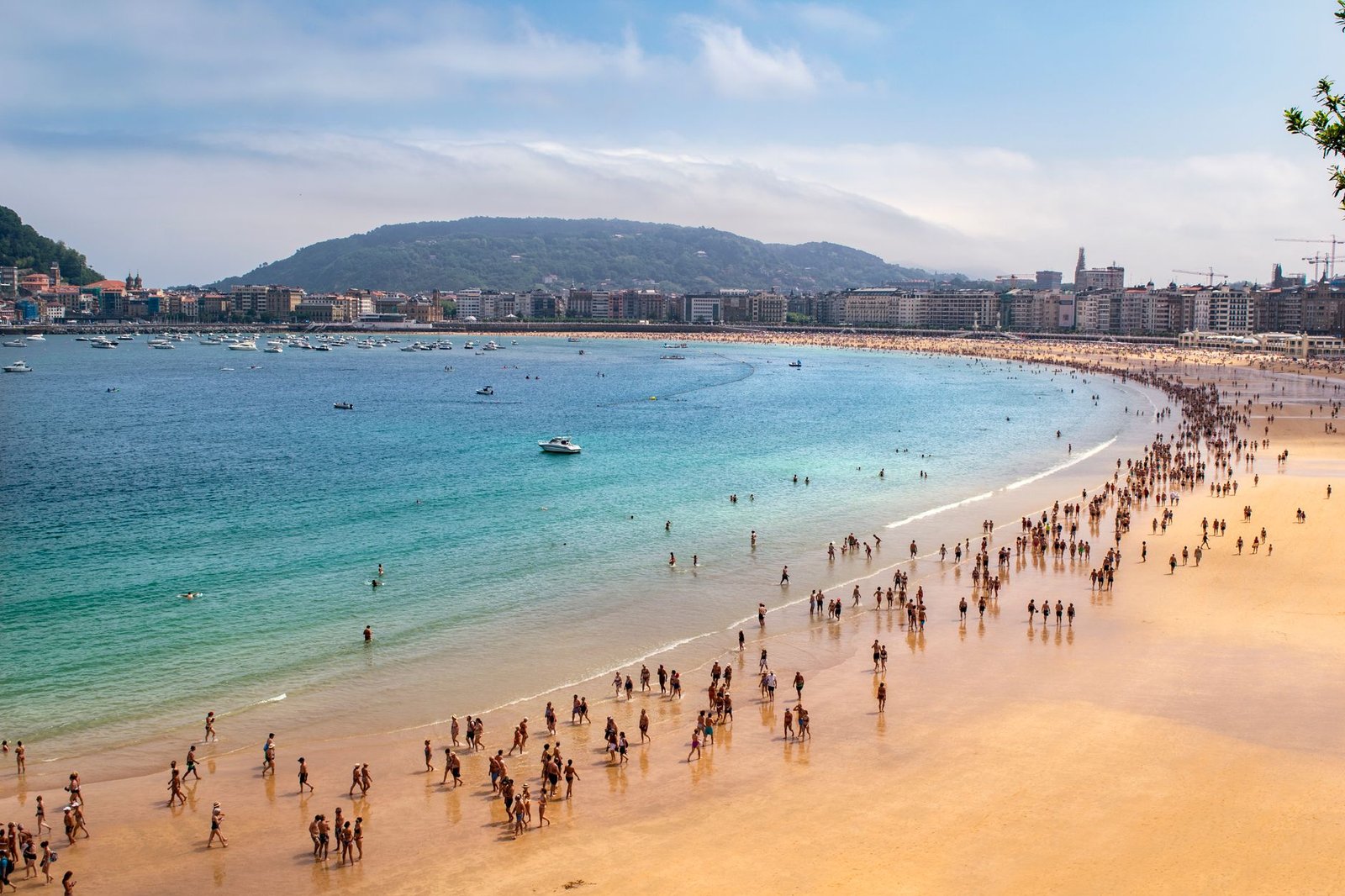 Crowds enjoy a day at San Sebastián beach with clear sky and turquoise water