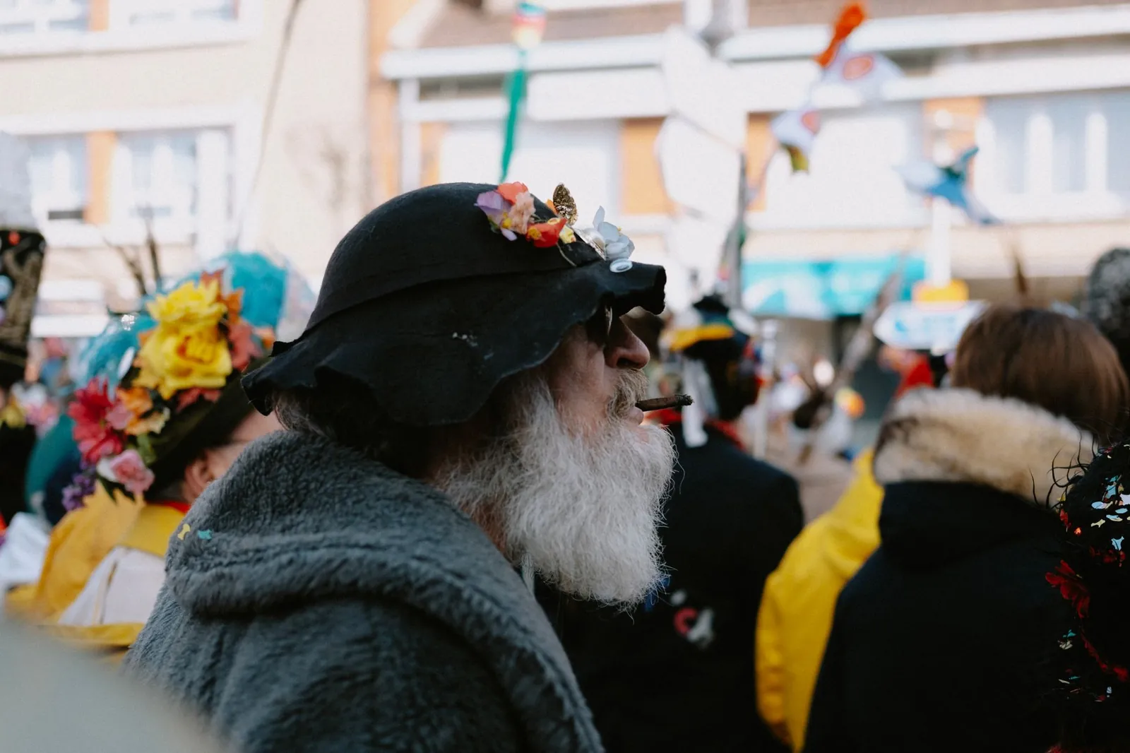 Elderly man with black hat and flowers smoking a cigar during a street parade