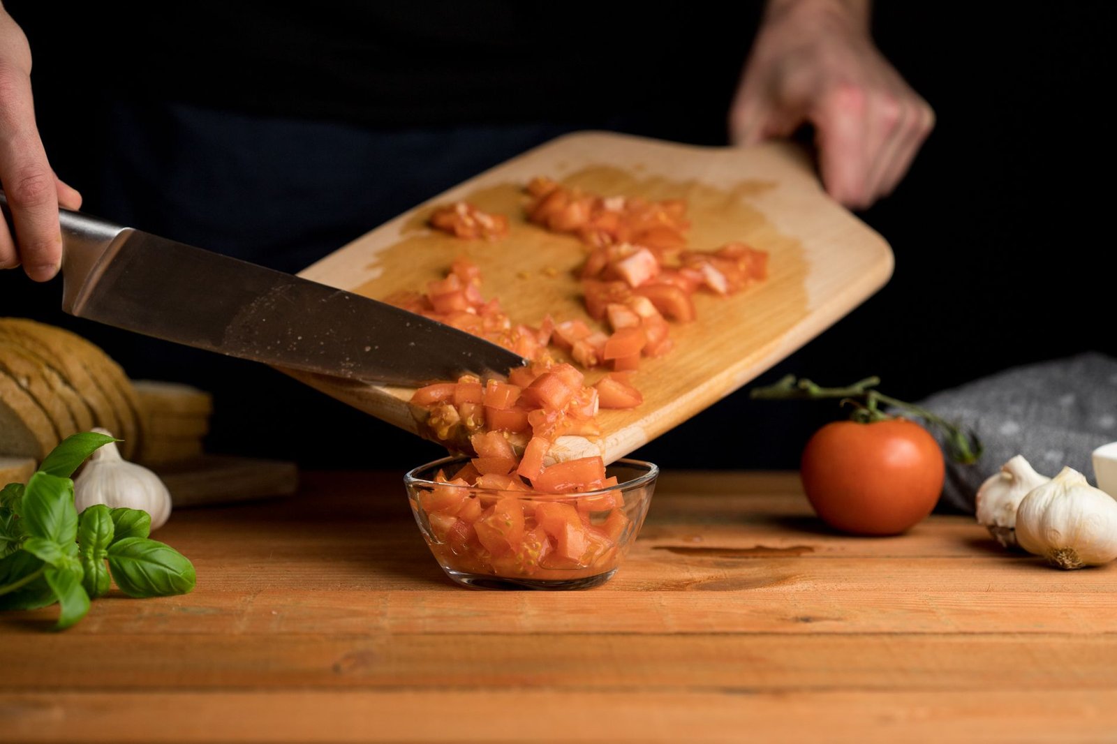 Chopped tomatoes being prepared on a wooden cutting board with fresh ingredients nearby