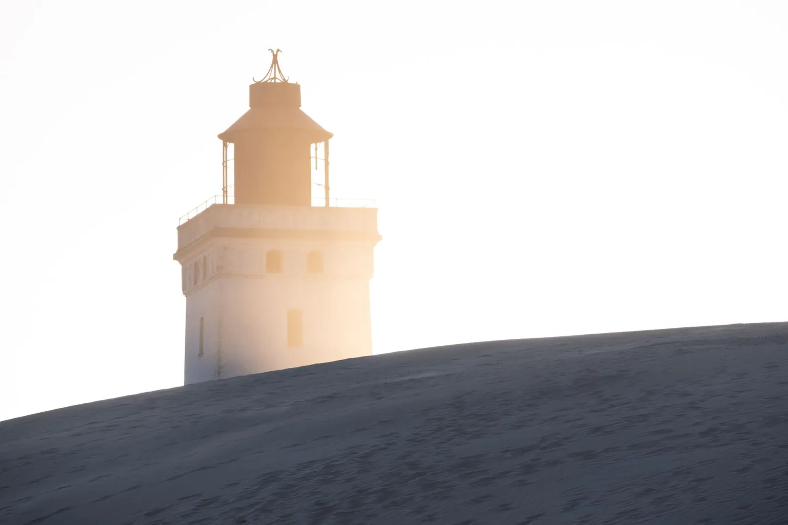 view of Rubjerg Knude Lighthouse at sunset with sand dunes in Denmark
