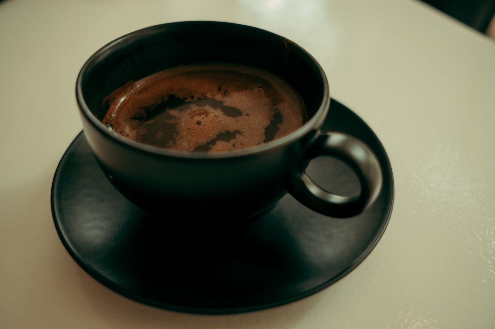 A close-up shot of a hot coffee in a black cup and saucer on a table, creating a cozy vibe