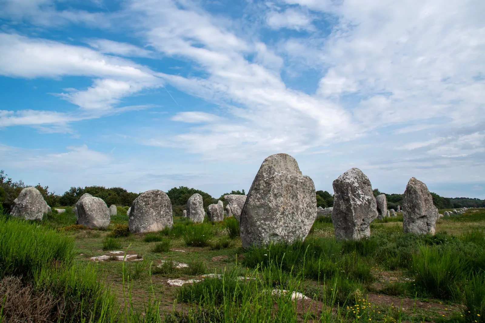 A series of ancient stone structures standing in a green field under a blue sky