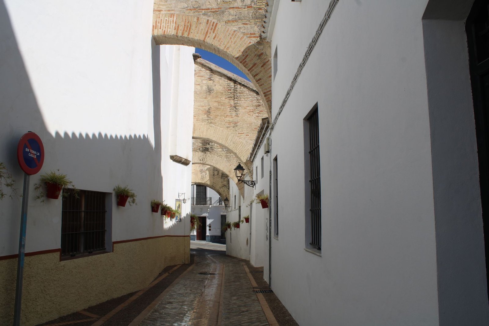 Explore a narrow street with white buildings and historical arches in Lebrija, Spain