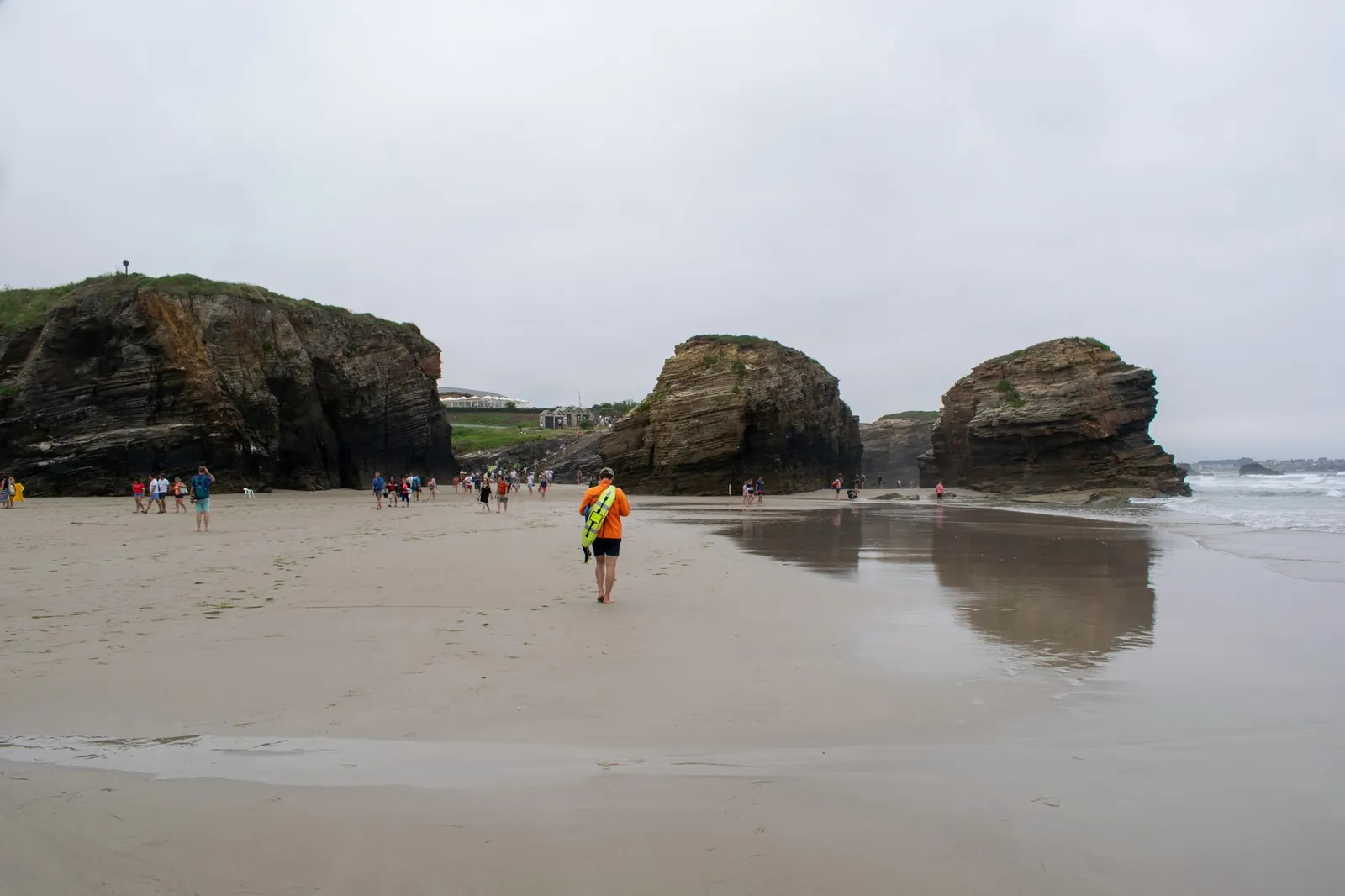 Tourists explore a sandy beach with striking rock formations under a cloudy sky