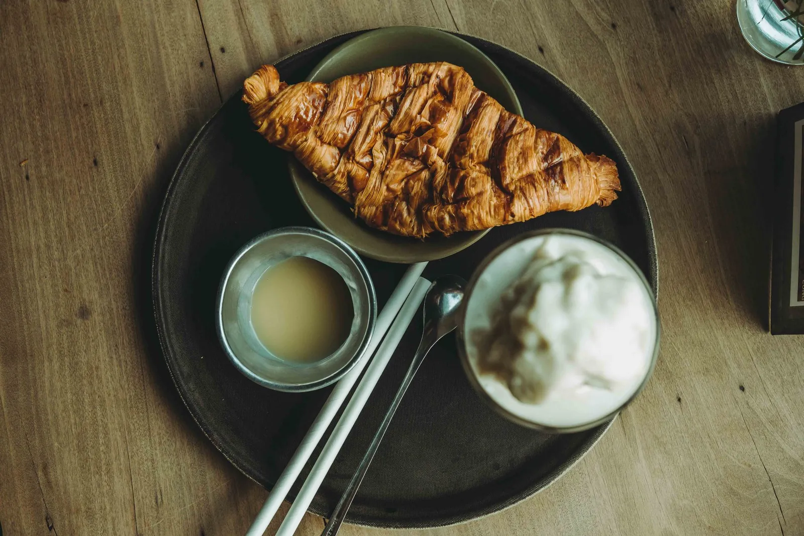 Flat lay of a croissant and coffee with cream on a wooden table, perfect for breakfast themes