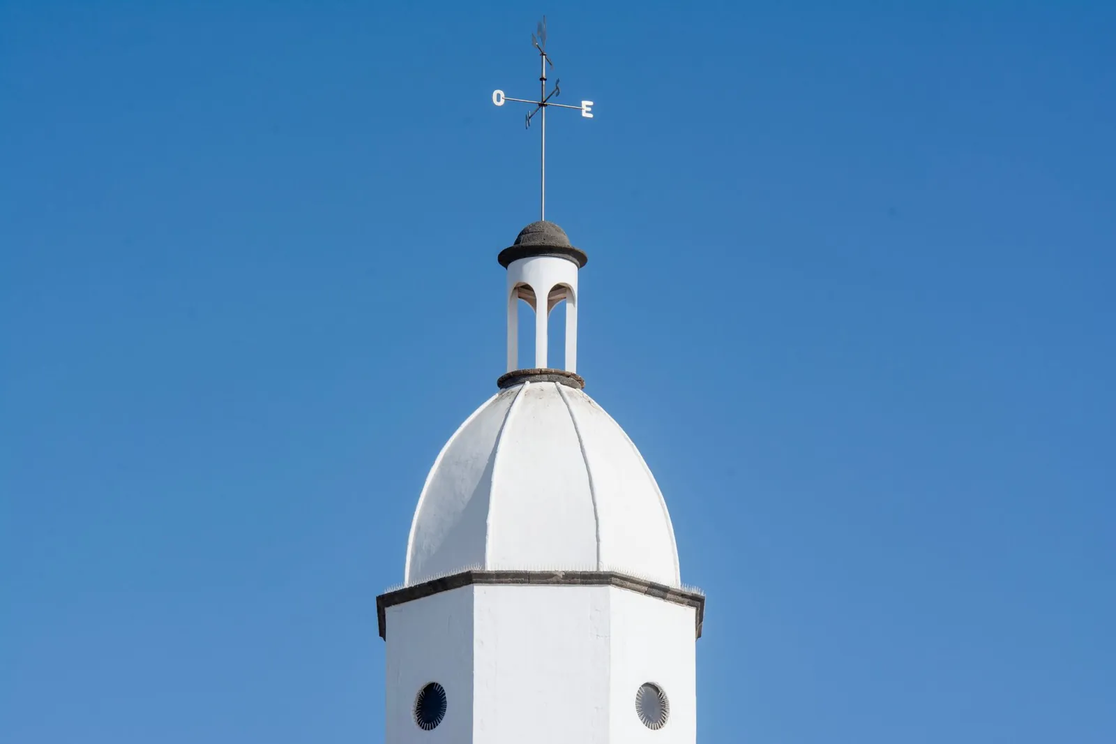 White bell tower with weather vane on top against a clear blue sky