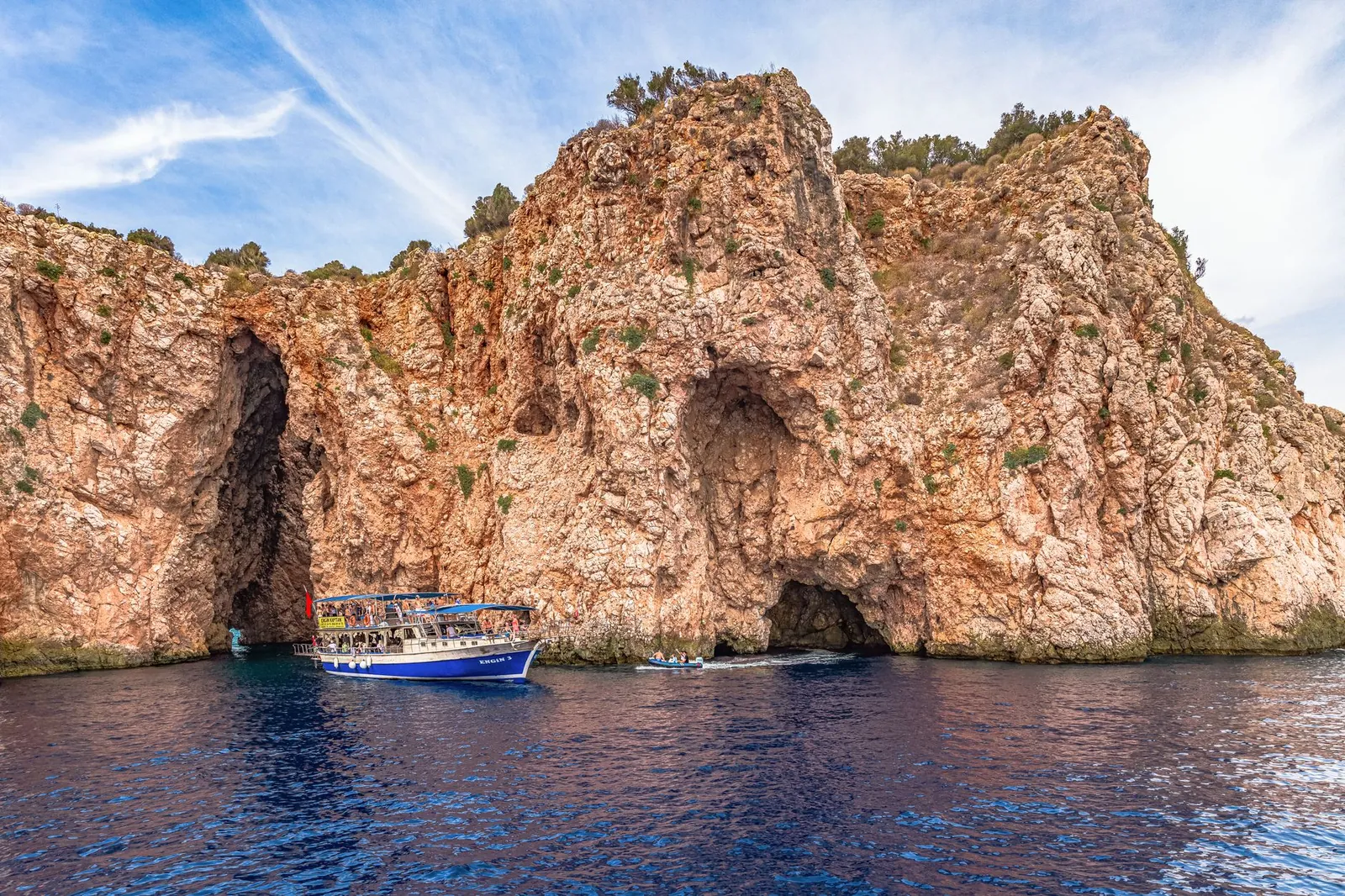 A boat navigating by rugged cliffs and sea caves in a coastal setting