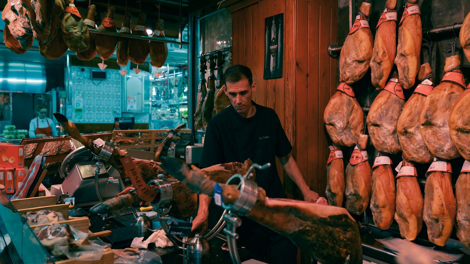 Man slicing Jamón in a traditional Barcelona market shop surrounded by hanging cured hams