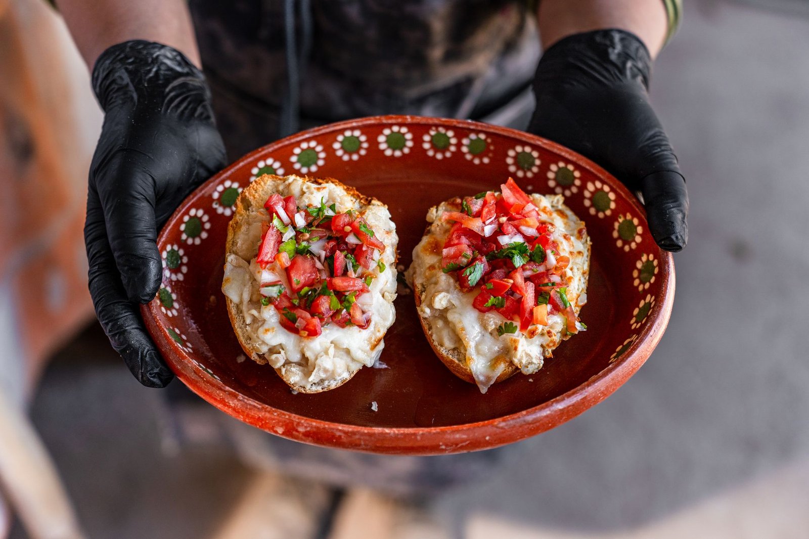 Close-up of traditional Mexican molletes topped with cheese and pico de gallo on a decorative plate