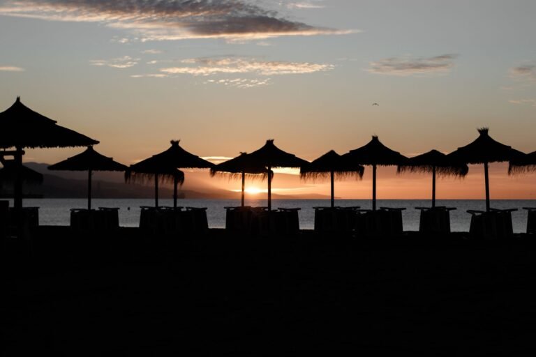 Sunset over the beach in Málaga, Spain, with straw umbrellas silhouetted against the colorful sky