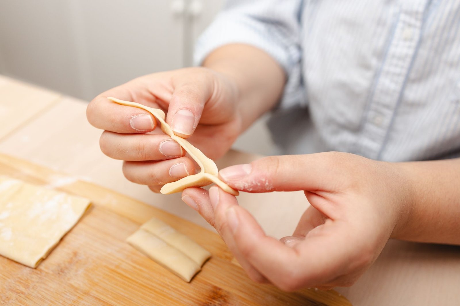 Hands skillfully shape fresh pasta dough on a wooden board in a cozy kitchen scene