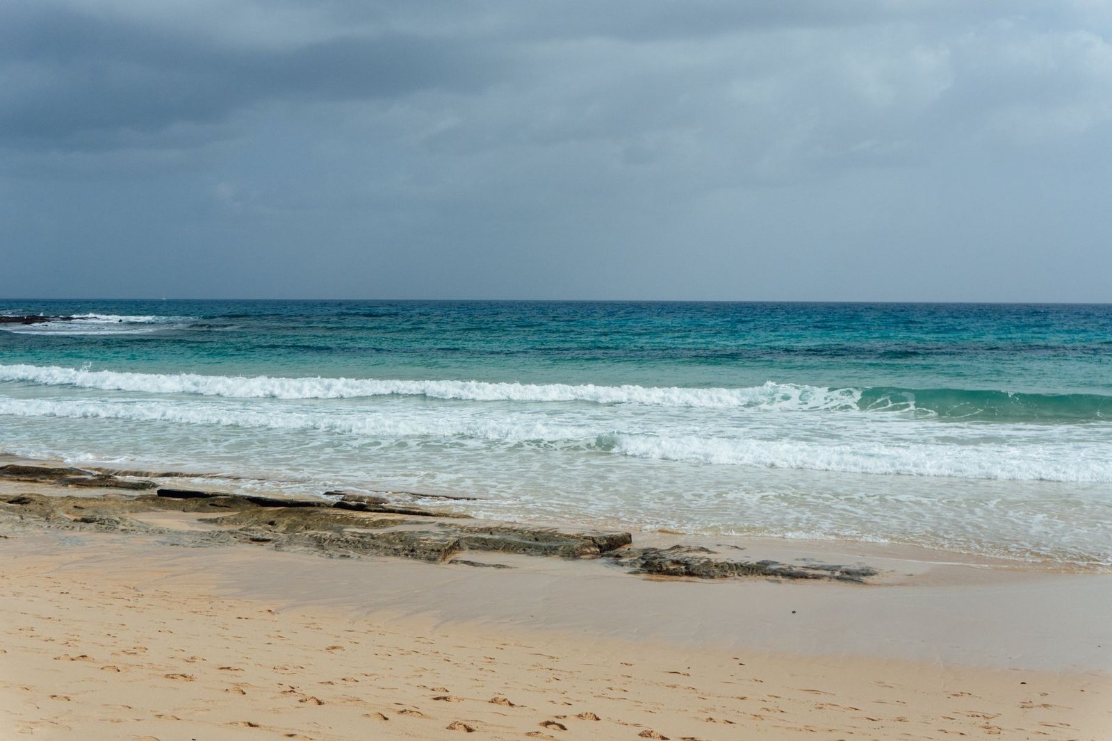 view of a sandy beach and blue ocean waves under a cloudy sky in the Canary Islands