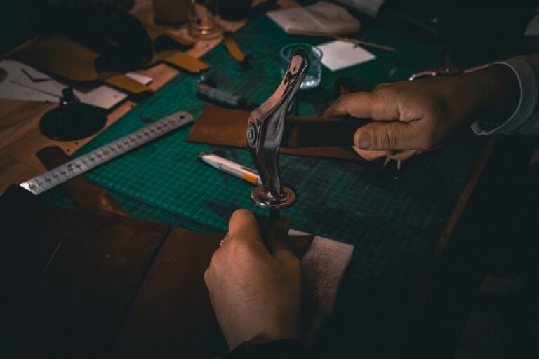 Hands crafting leather with tools on a workbench under warm lighting, showcasing artisanal skill