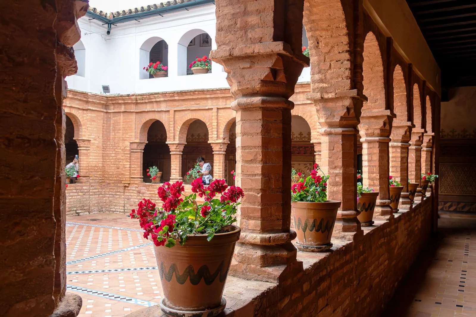 Colorful courtyard featuring red flowers in pots, surrounded by traditional brick arches