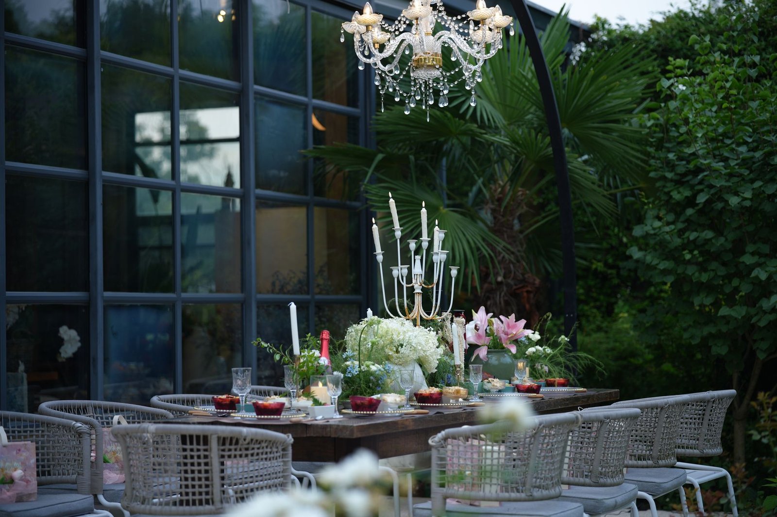 A beautifully set outdoor dining table with chandeliers and floral decorations, perfect for summer gatherings
