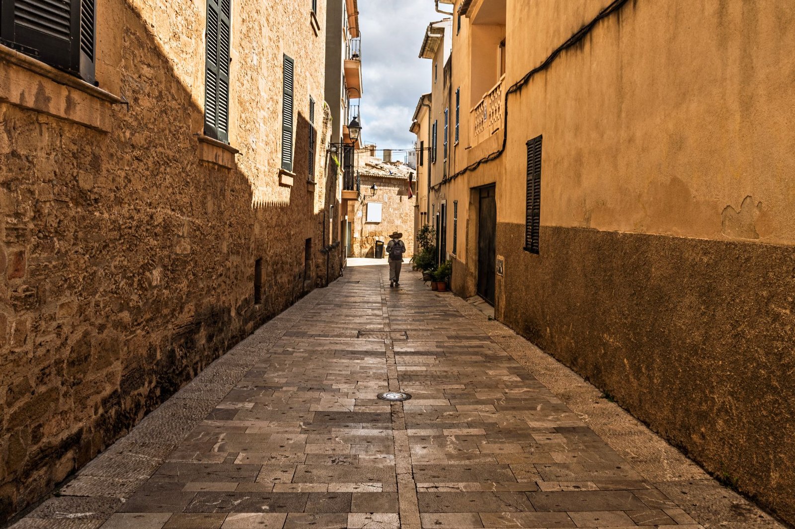 Beautiful narrow street in Alcúdia, Spain, showcasing rustic architecture and a lone pedestrian