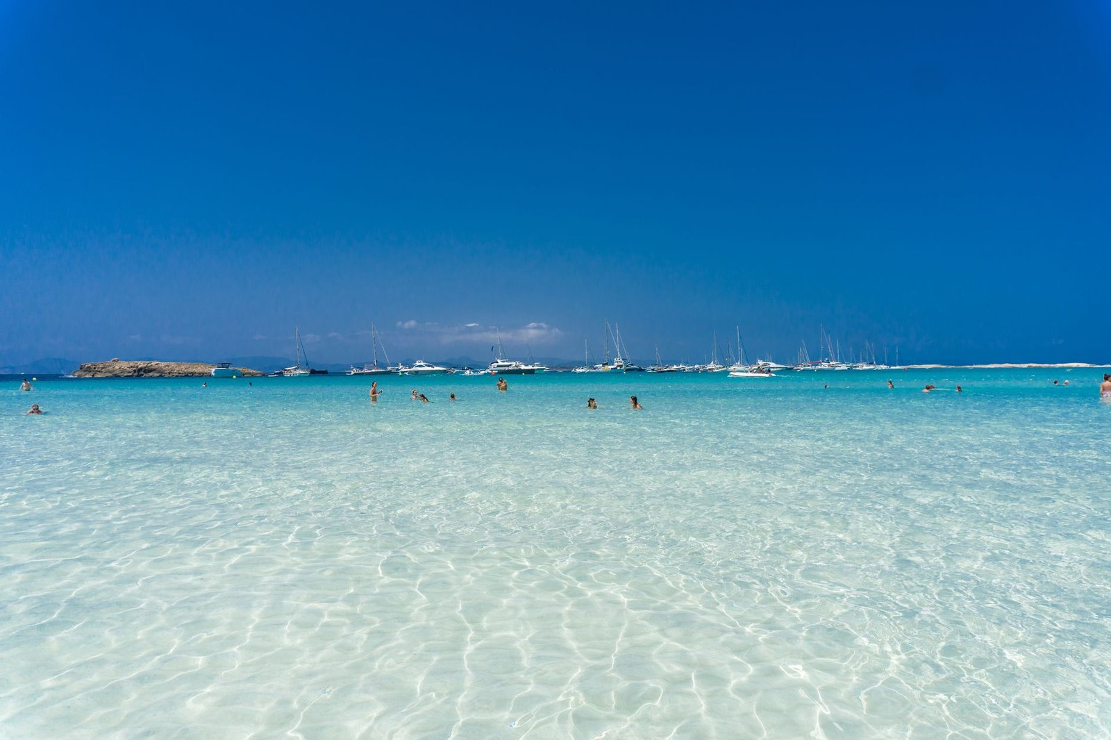 Enjoy leisure time at a Spanish beach with turquoise waters and distant yachts, perfect for summer vacation