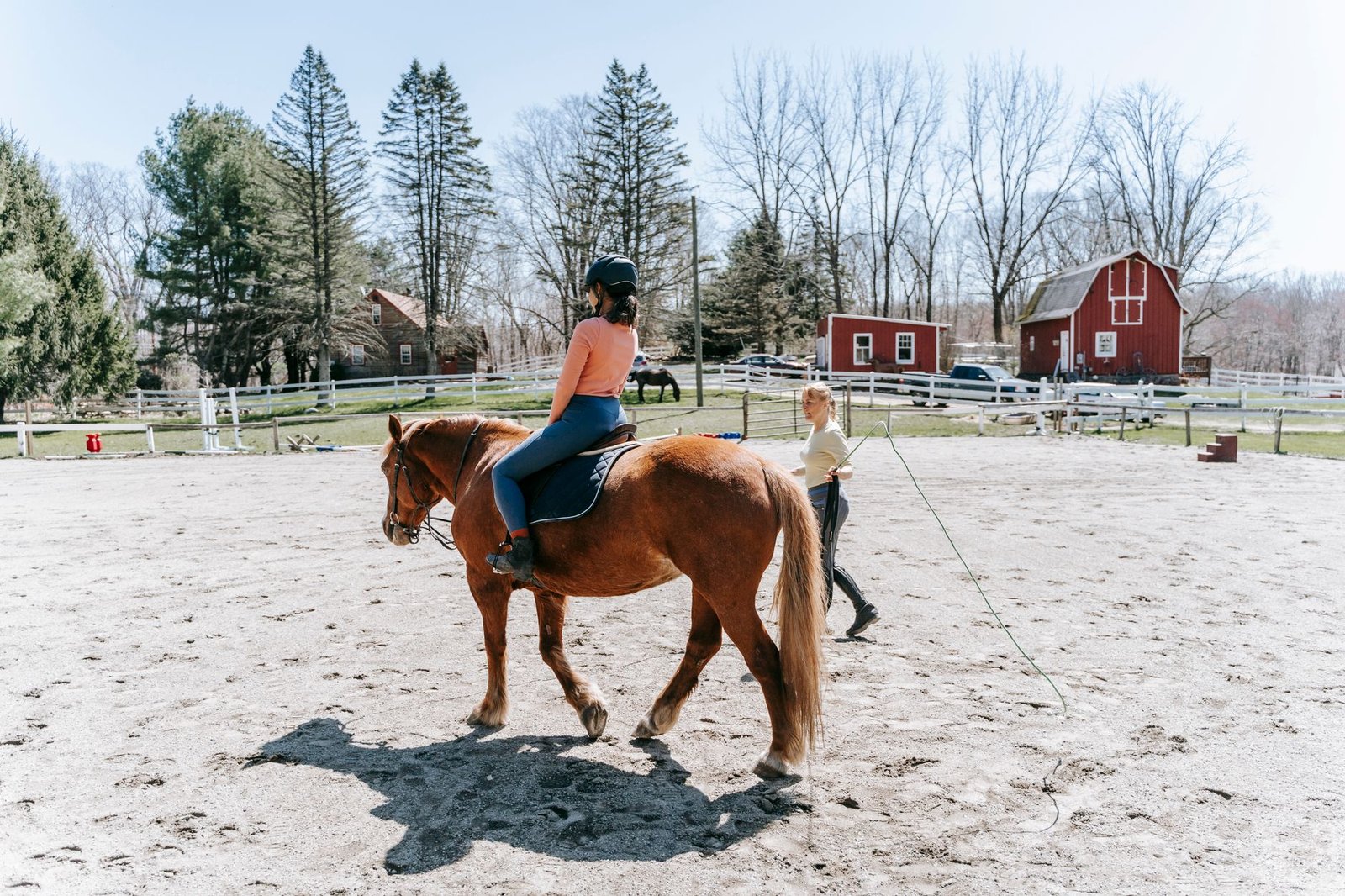 A woman learning horseback riding in an outdoor arena with instructor guidance