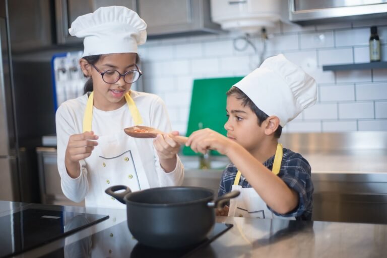Two young children in chef hats cooking together in a modern kitchen setting