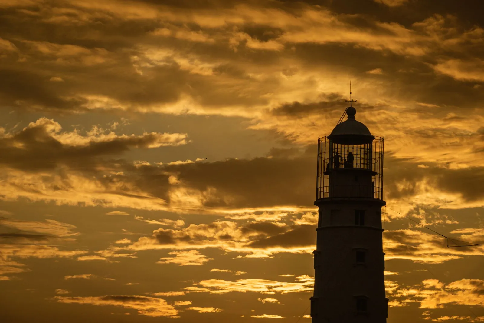 A dramatic silhouette of a lighthouse against a golden sunset sky