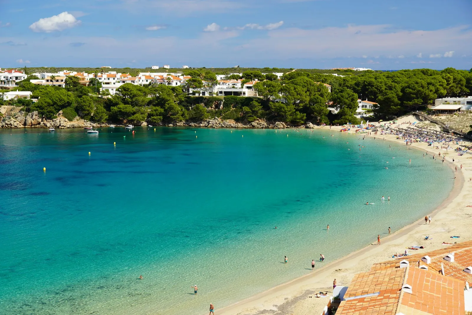 A view of a beach in Menorca with clear waters and greenery
