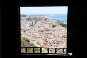 Aerial view of an urban coastal city through a window frame, showcasing buildings and the sea